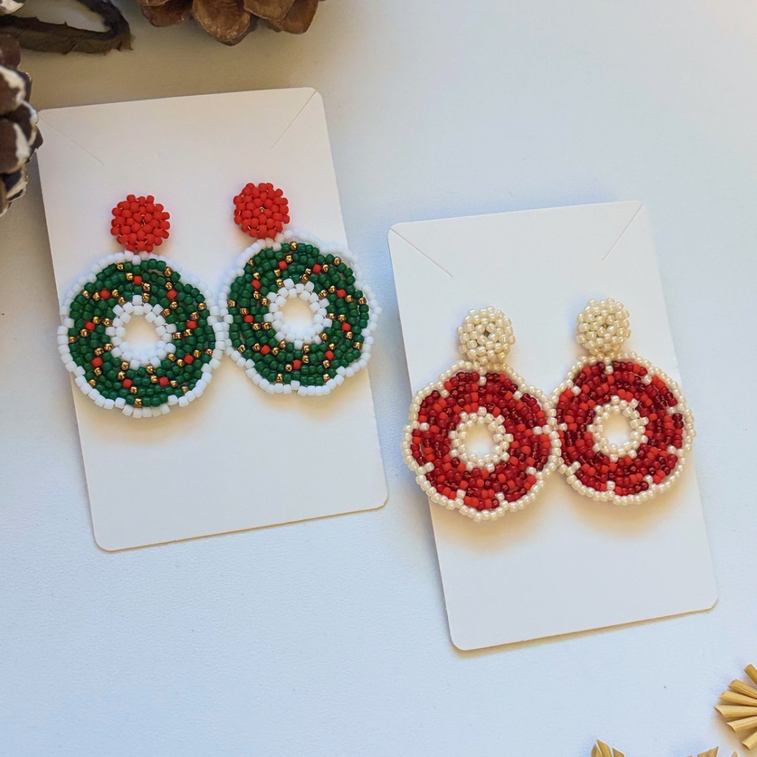 Cercei handmade lucrați manual în formă de coroniță de Crăciun, din mărgele verzi, roșii și crem, prezentați pe suport – bijuterii festive de iarnă, ideale pentru sărbători și cadouri de Crăciun.