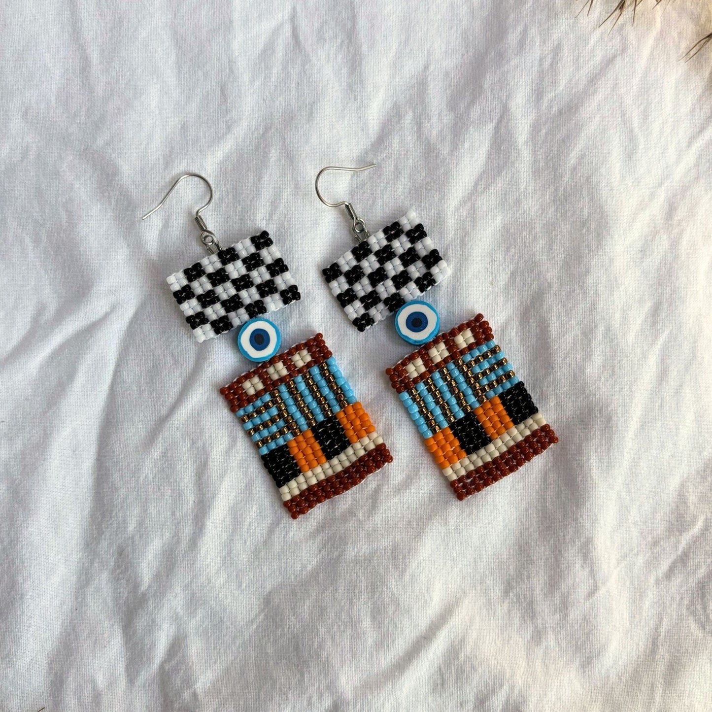 Cercei artizanali, lucrati manual din margele fine, design geometric perfect pentru stilul urban, detaliu ochi protector albastru cu alb, combinatie negru, turcoaz, portocaliu si detalii aurii, cercei statement etnici, bijuterii handmade unicat, boho contemporan, accesorii originale pentru tinute creative.