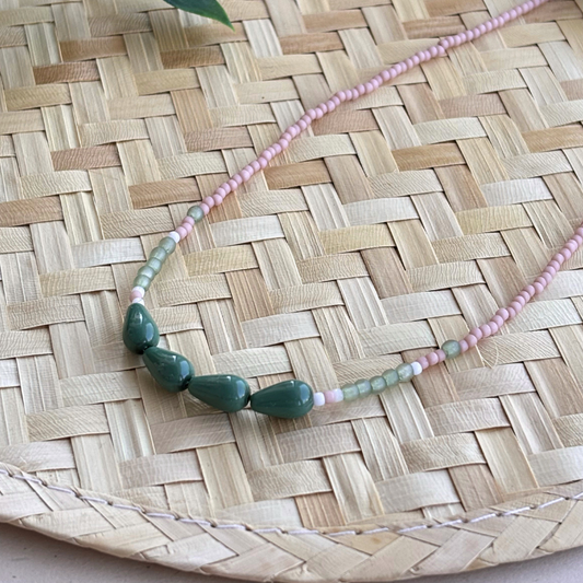 Colier subtire la baza gatului din margele pastelate roz si verde salvie accentuat cu patru margele mari verzi in forma de picatura asezat pe suport din ratan