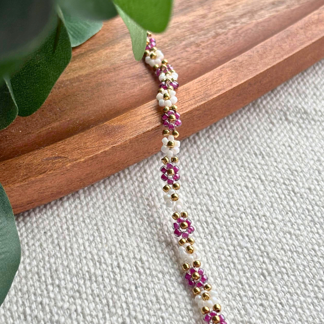 Bratara Martisor handmade cu floricele din margele mov si albe, completata cu accente aurii. Cadou delicat de primavara, feminin si usor de asortat.