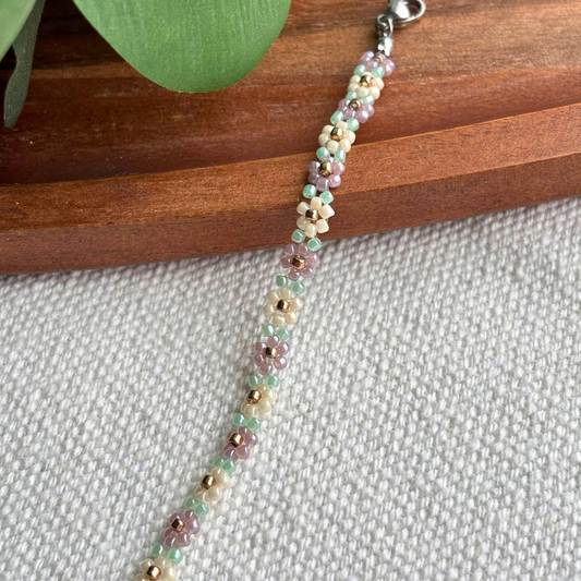 Bratara Martisor handmade cu floricele din margele in nuante pastel (verde menta, lila, crem) si accente aurii. Cadou delicat de primavara, usor de purtat zilnic.