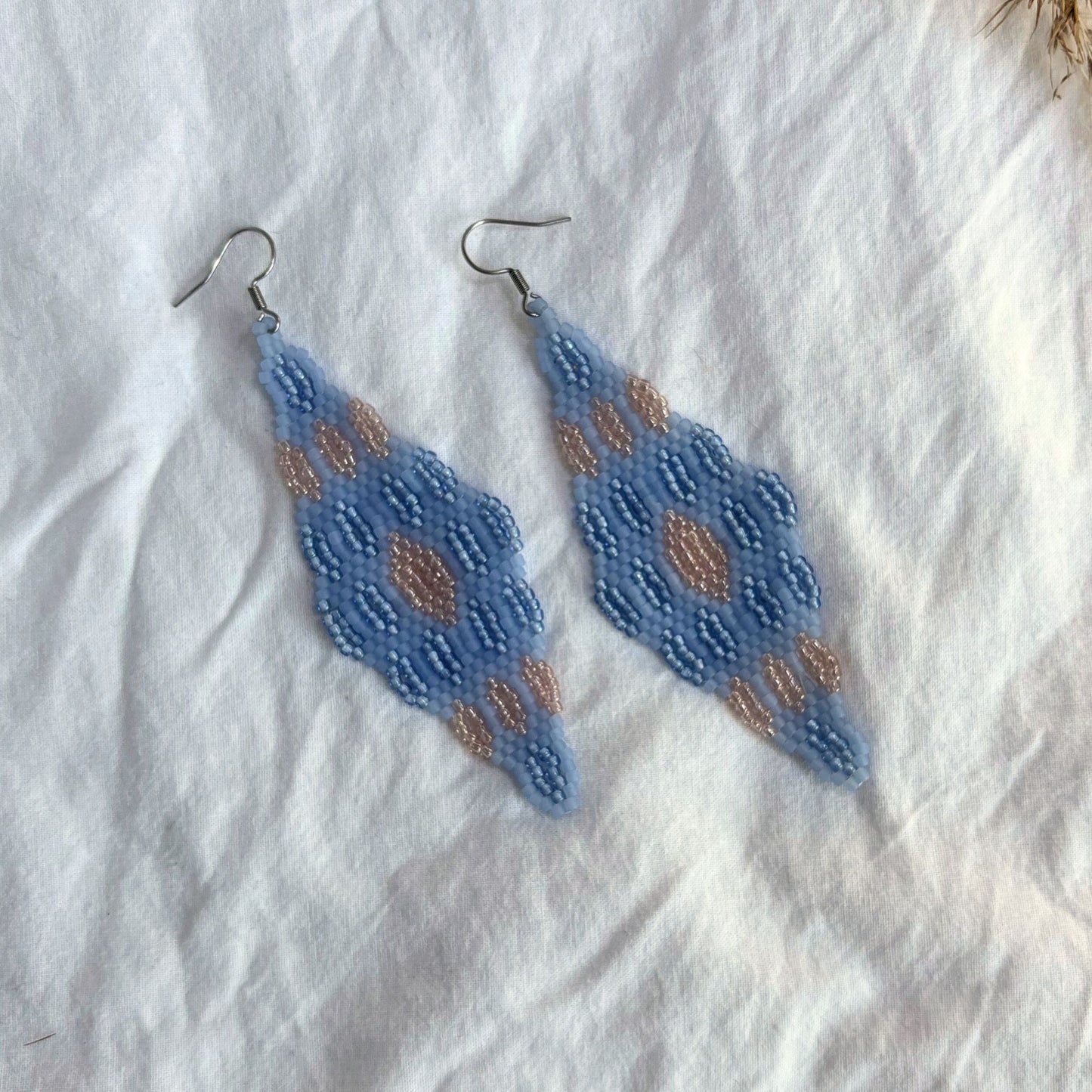 Cercei handmade lungi din mărgele fine în nuanțe de albastru deschis cu accente bej-aurii, design geometric tip romb, cercei statement ușori, stil boho și elegant, bijuterii artizanale unicat potrivite pentru ținute de zi sau evenimente speciale.