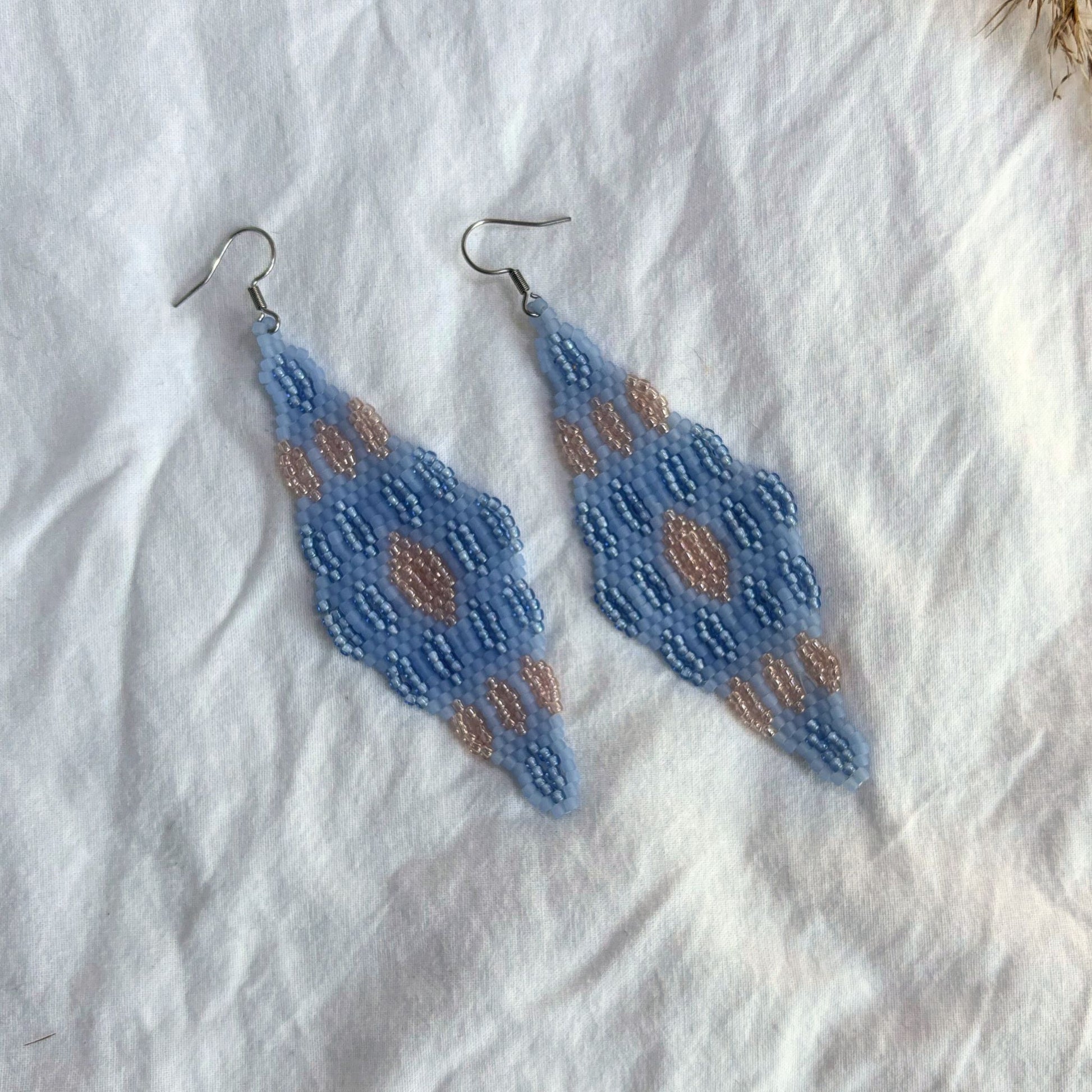 Cercei handmade lungi din mărgele fine în nuanțe de albastru deschis cu accente bej-aurii, design geometric tip romb, cercei statement ușori, stil boho și elegant, bijuterii artizanale unicat potrivite pentru ținute de zi sau evenimente speciale.