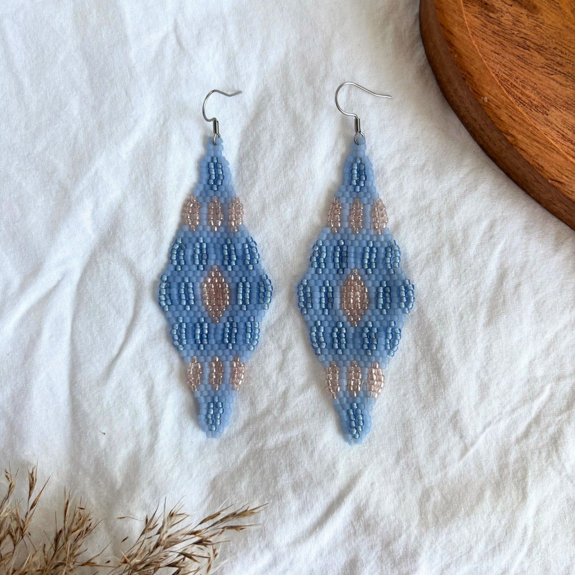 Cercei handmade lungi realizați din mărgele fine în nuanțe de albastru pastel și accente roz, design geometric simetric tip romb, cercei statement ușori, stil boho-elegant, bijuterii artizanale unicat potrivite pentru ținute de zi, vară și evenimente speciale.