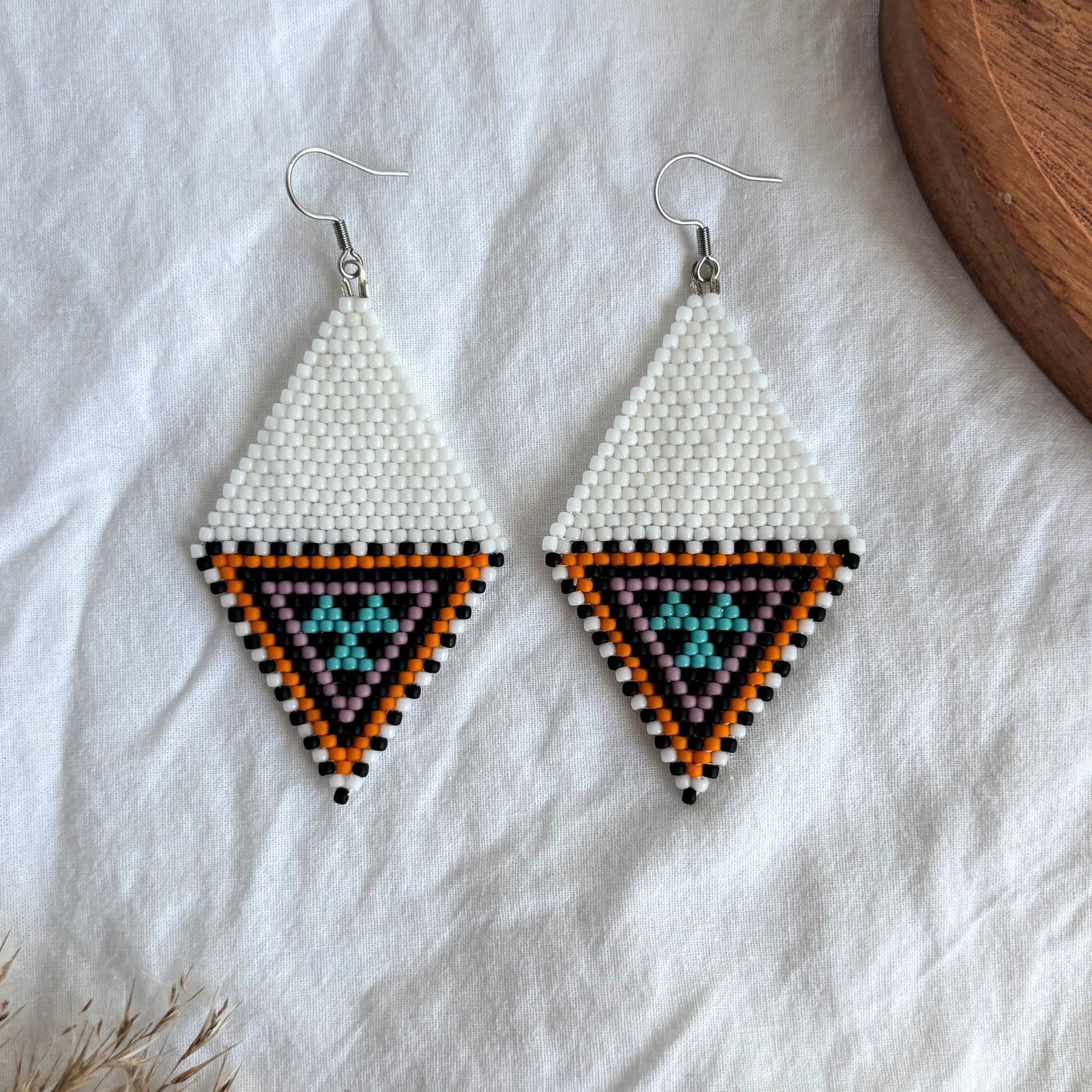 Cercei handmade romb, realizați din mărgele fine în nunțe de alb, portocaliu, negru și turcoaz, design geometric tip romb, cercei statement ușori, stil boho-elegant, bijuterii artizanale unicat potrivite pentru ținute de zi, vară și evenimente speciale.