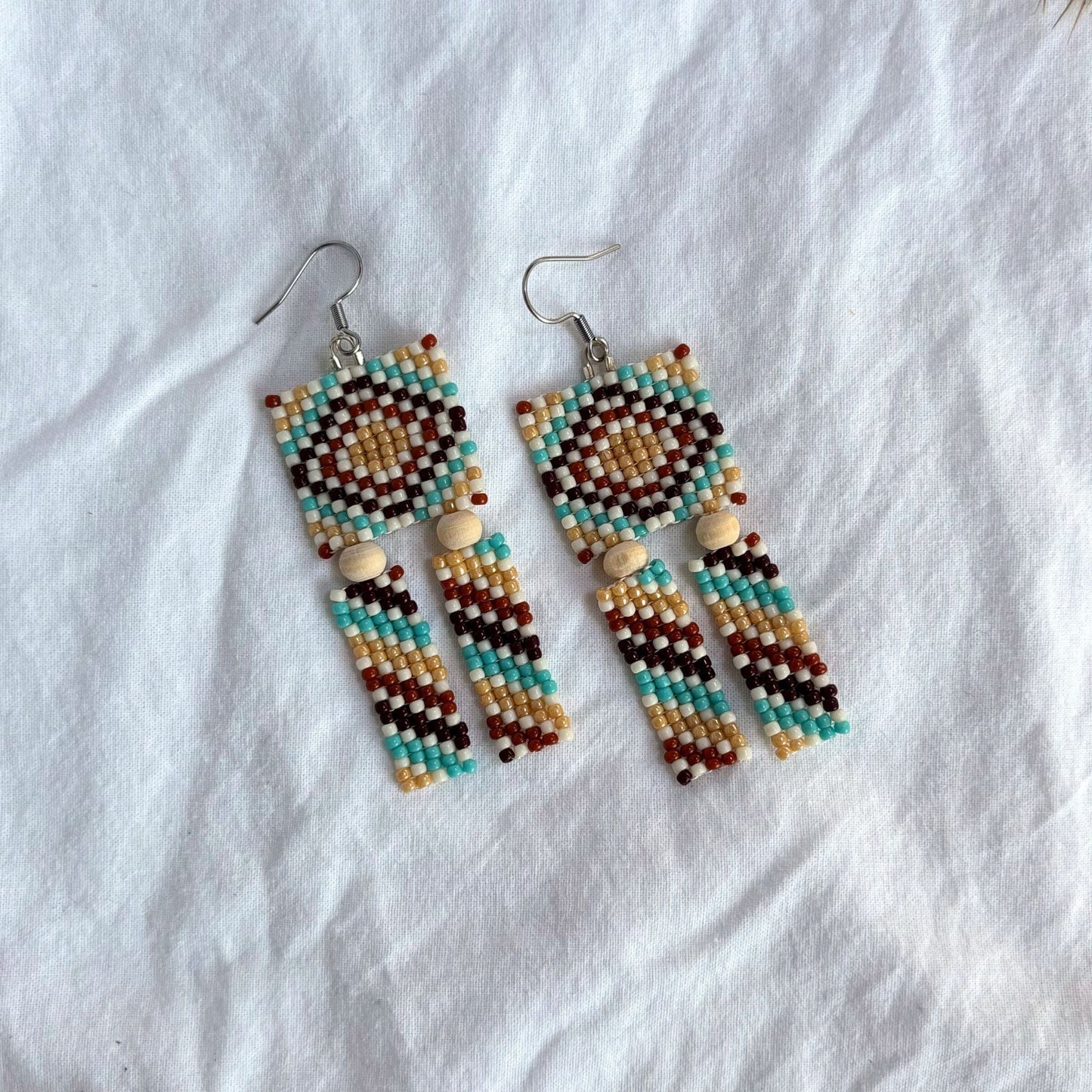 Cercei handmade din mărgele, cu design geometric multicolor în nuanțe de turcoaz, bej, maro și alb, cercei lungi stil boho cu mărgele mici și elemente din lemn, bijuterii artizanale ușoare, potrivite pentru ținute casual, de vară sau festival.