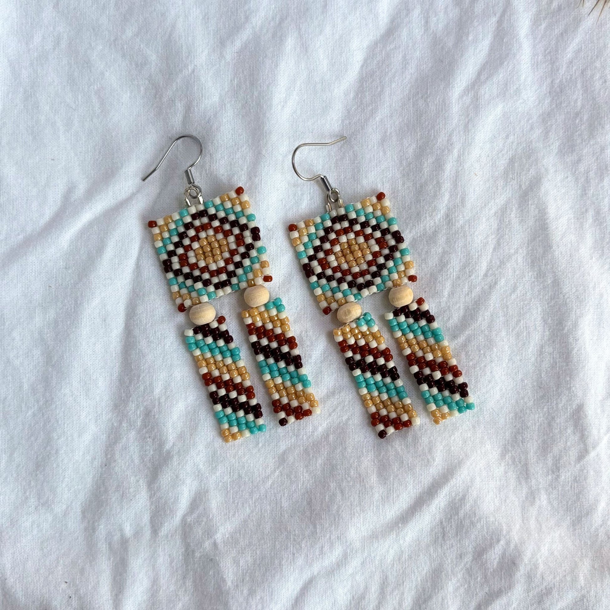 Cercei handmade din mărgele, cu design geometric multicolor în nuanțe de turcoaz, bej, maro și alb, cercei lungi stil boho cu mărgele mici și elemente din lemn, bijuterii artizanale ușoare, potrivite pentru ținute casual, de vară sau festival.