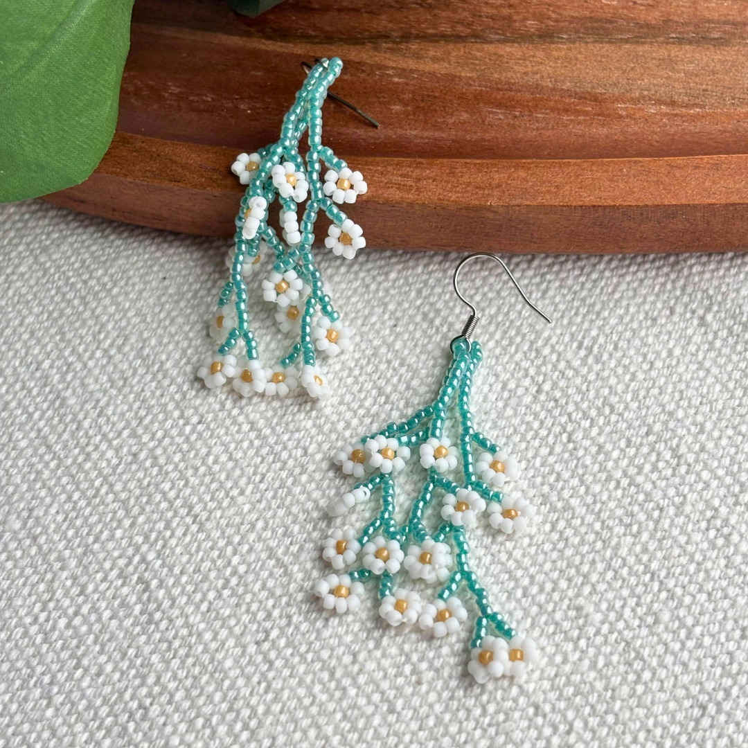 Cercei lungi realizați manual din mărgele de sticlă, model ramură florală turcoaz cu flori albe și detalii aurii, bijuterii handmade ușoare pentru ținute de primăvară și cadou de martisor.