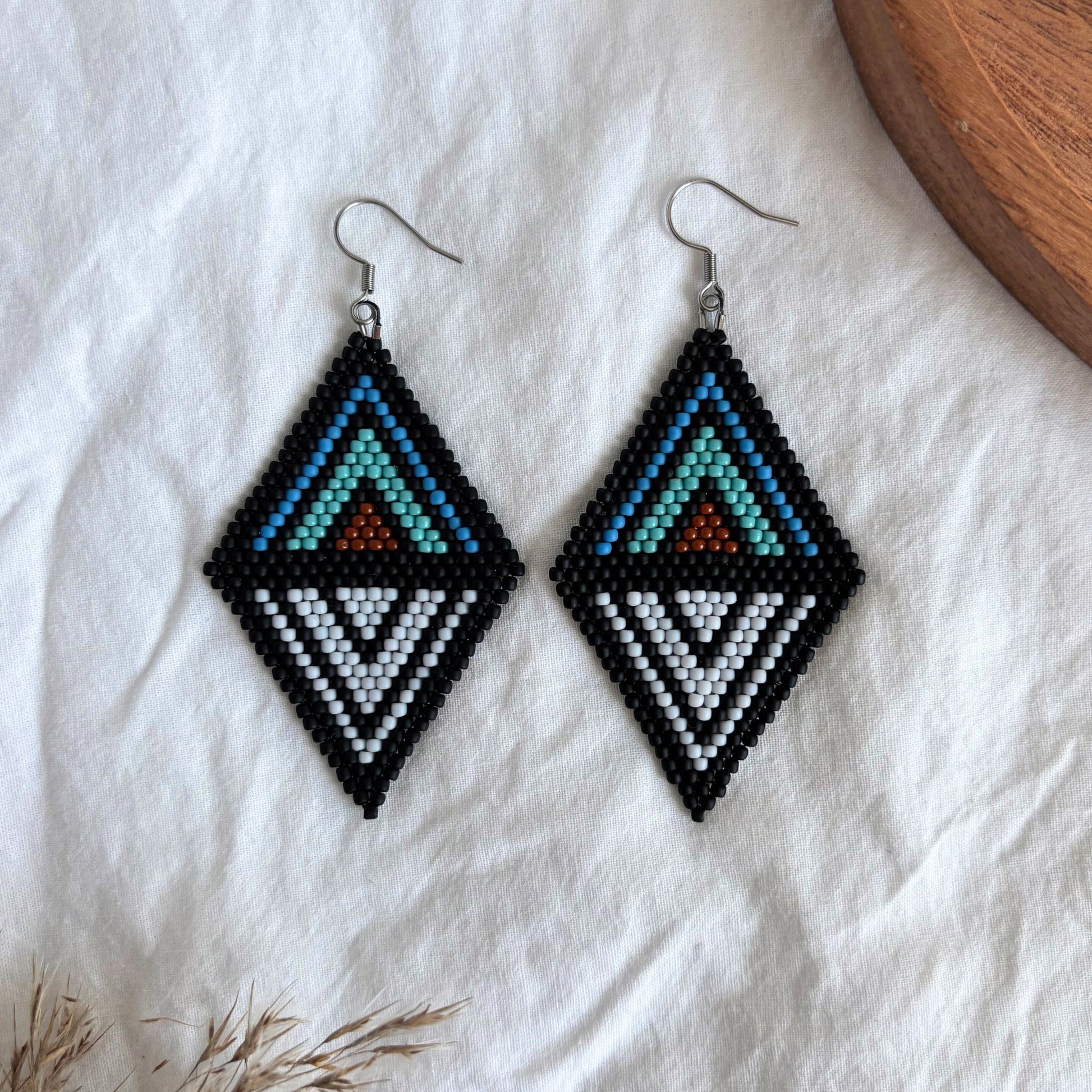 Cercei realizați manual din mărgele fine, cu design geometric elegant tip romb, în nuanțe de negru, alb, albastru, turcoaz și cărămiziu, accesorii statement pentru inute casual, de vară sau ocazii speciale, bijuterii artizanale unicat.