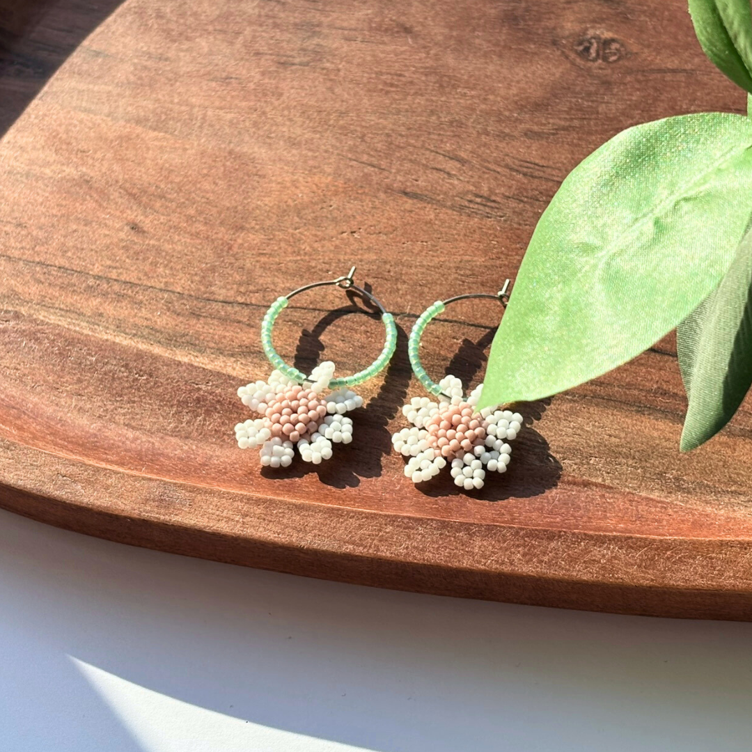 Cercei tip hoops handmade, cu cerc verde mentă din mărgele și floricele din mărgele albe cu centru roz pudrat – bijuterii florale de primăvară/vară, ideale pentru cadou.