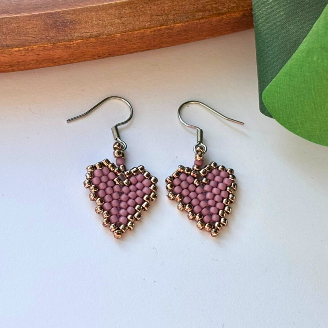 Cercei handmade în formă de inimă, realizați din mărgele lila prăfuit cu margine aurie, cu tortițe metalice – bijuterii delicate, ideale pentru cadou.