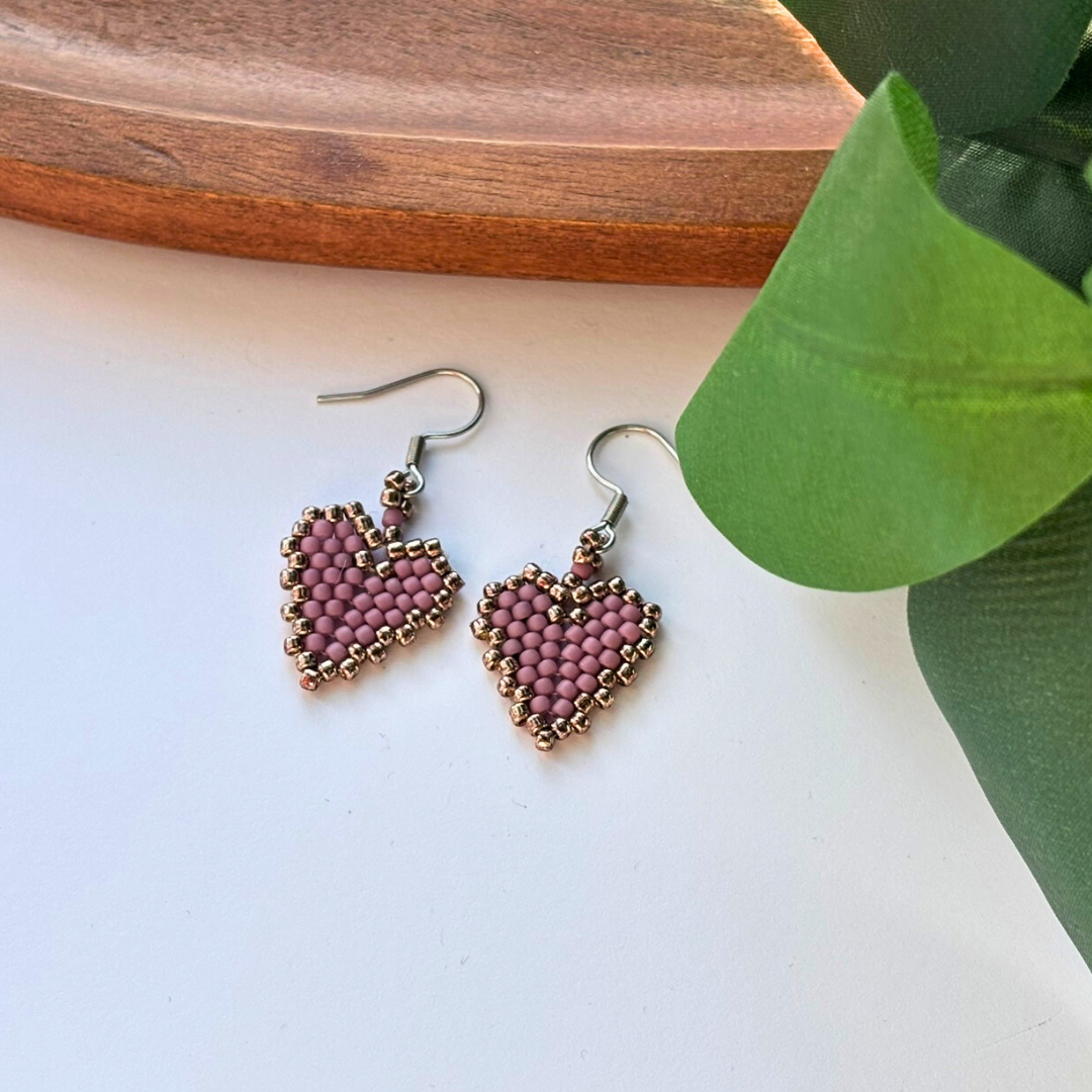 Cercei handmade în formă de inimă, din mărgele lila prăfuit cu margine aurie, pe tortițe argintii – bijuterii delicate, cadou romantic.