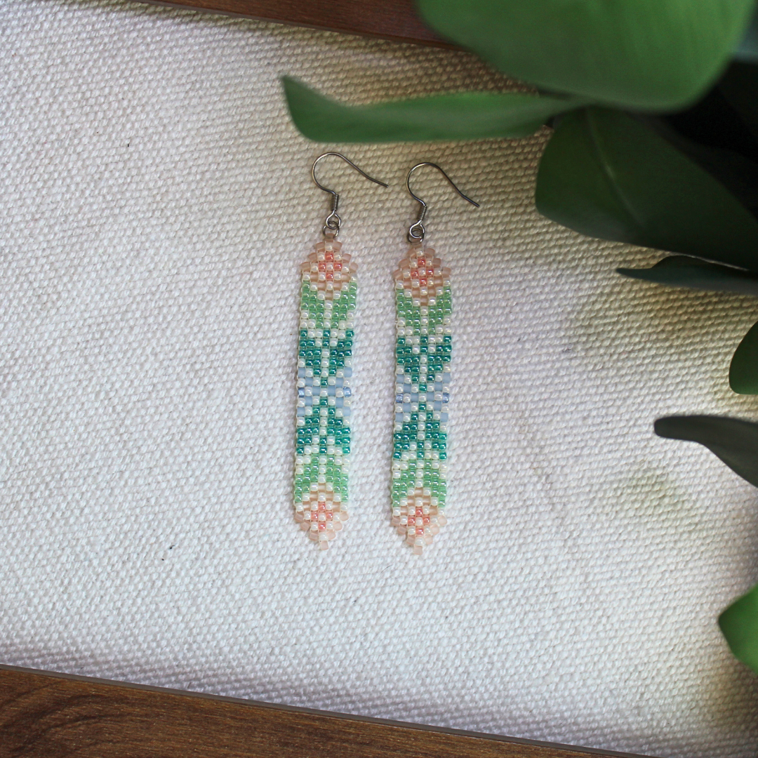 Cercei handmade lungi din mărgele în nuanțe pastel de verde, albastru și roz, cu model geometric fin și agățătoare metalică, bijuterii artizanale ușoare, elegante și moderne, potrivite pentru ținute boho, casual sau de vară.