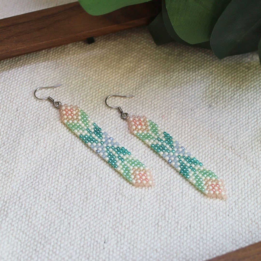 Cercei handmade lungi din mărgele mici, în nuanțe pastel de verde, albastru și roz, cu design geometric fin și agățătoare metalică, bijuterii artizanale ușoare și elegante, ideale pentru ținute boho, de vară sau cadou special.