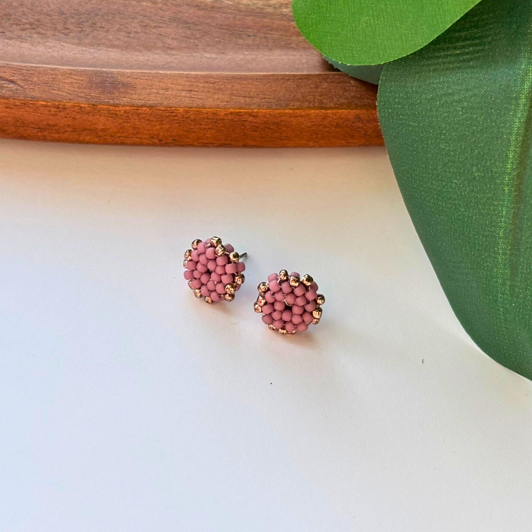 ercei lucrati manual tip stud, rotunzi, realizați din mărgele roz prăfuit cu margine aurie, pe fundal natural – bijuterii delicate și elegante, potrivite pentru purtare zilnică sau cadou.