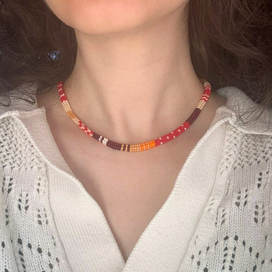 Colier choker la baza gatului handmade lucrat manual din mărgele fine în nuanțe de roșu, portocaliu, maro și crem, purtat la gât, design etnic-boho – bijuterie ușoară, perfectă pentru ținute casual, de vară sau cadou special.