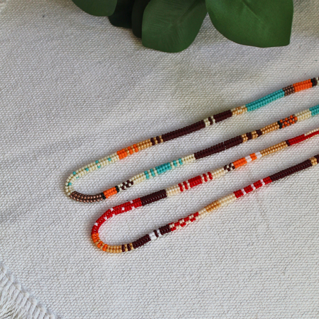 Set de coliere handmade lucrate manual din mărgele fine în nuanțe de roșu, portocaliu, maro, crem și turcoaz, design boho-etnic, așezate pe material textil – bijuterii ușoare, ideale pentru layering, ținute casual sau cadou.