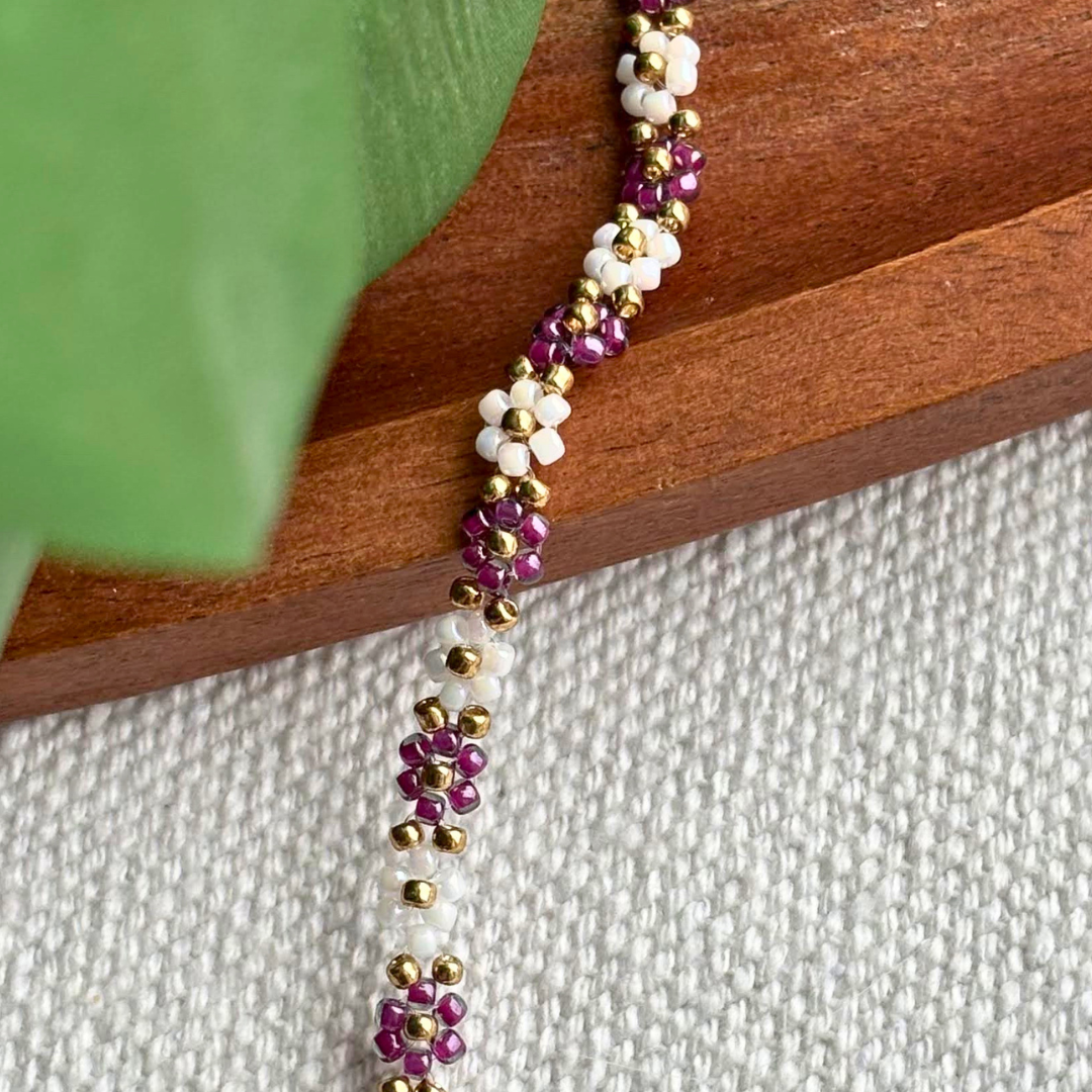 Martisor bratara eleganta lucrata manual, cu flori din margele mov si albe si accente aurii. Ideala pentru cadou de 1-8 Martie sau purtare zilnica.