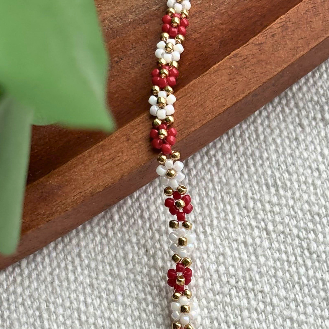 Martisor bratara fina lucrata manual, cu flori rosii si albe din margele si accente aurii. Ideala pentru un cadou elegant si usor de purtat zilnic.