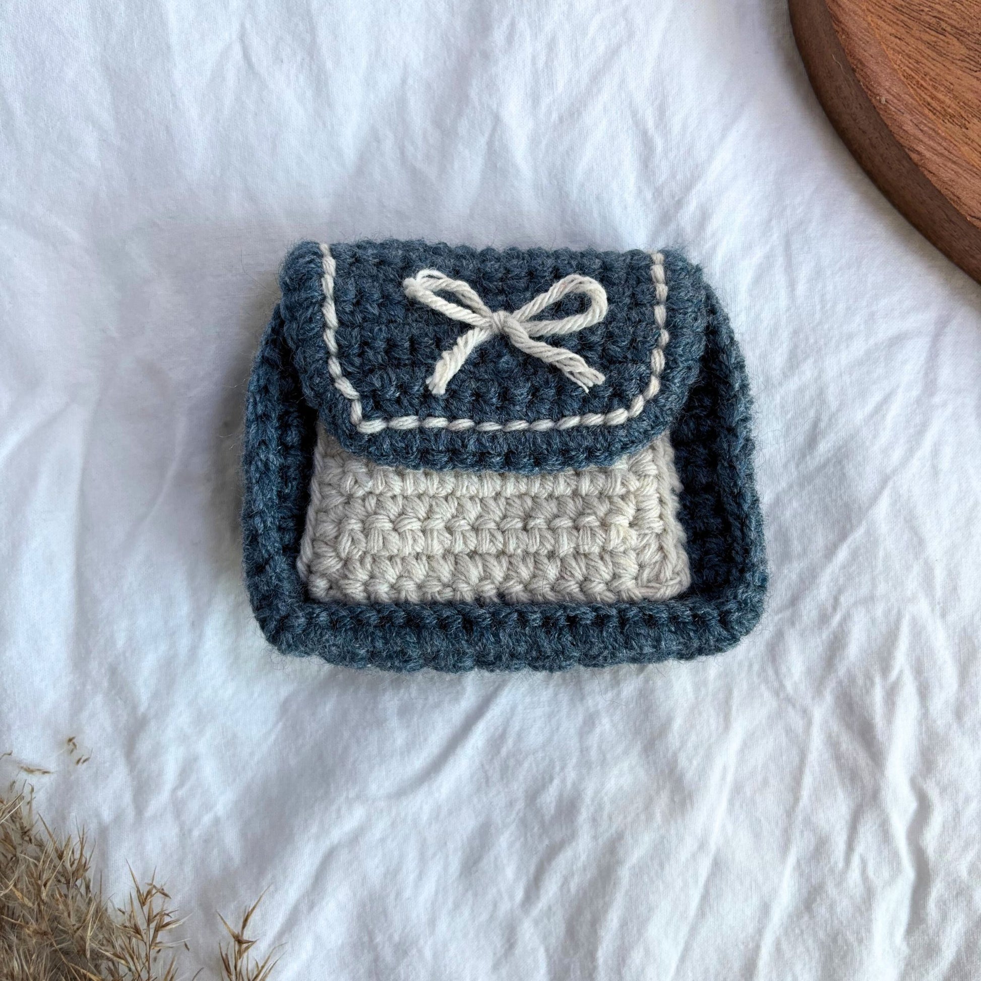 Punguță croșetată handmade în nuanțe de albastru și crem, realizată manual din fir textil, cu clapetă și fundiță decorativă, ideală pentru cadouri mici, bijuterii sau accesorii, design minimalist și natural.