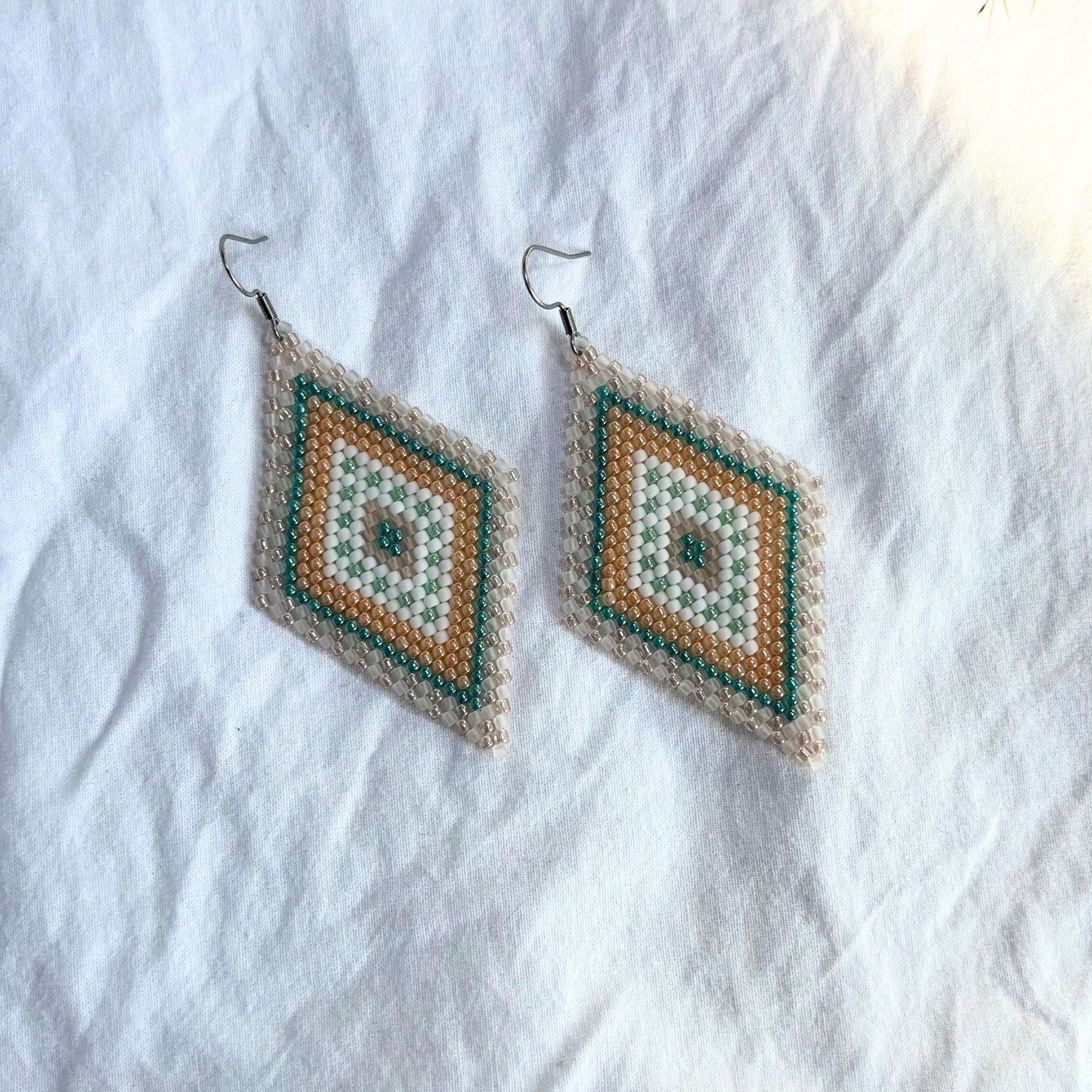 Cercei lungi lucrați manual din margele delicate, în nuante pastel de turcoaz, roz, portocaliu si alb, design geometric tip romb, cercei statement usori, stil boho si elegant, bijuterii artizanale unicat potrivite pentru tinute de zi, evenimente speciale sau cadou.